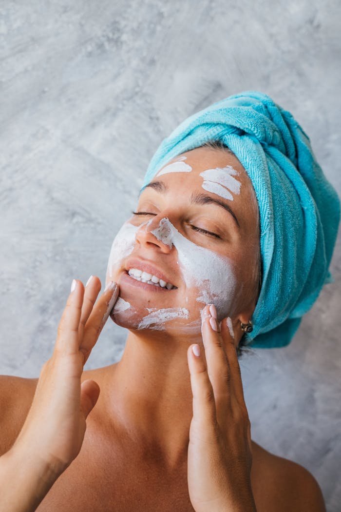 Woman with a face mask and towel, enjoying skincare pampering session indoors.