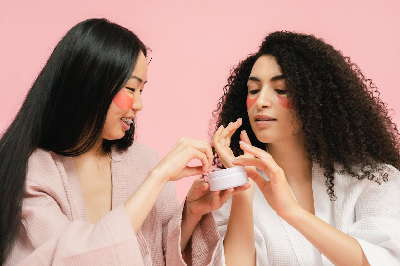 Two women with facial patches apply skincare cream, enhancing beauty and self-care routine.